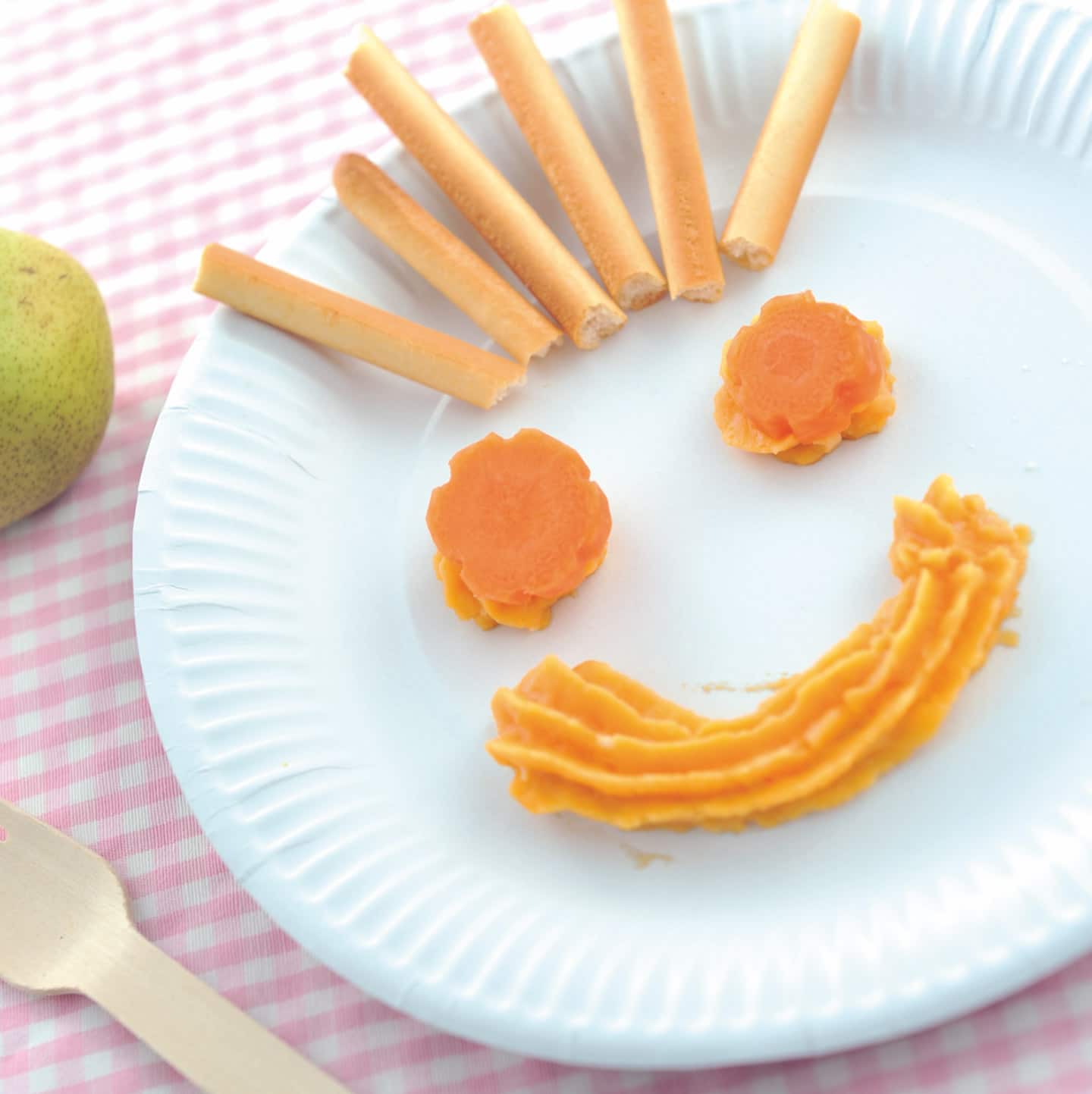 A babys plate with a smiling face made out of carrots and bredsticks