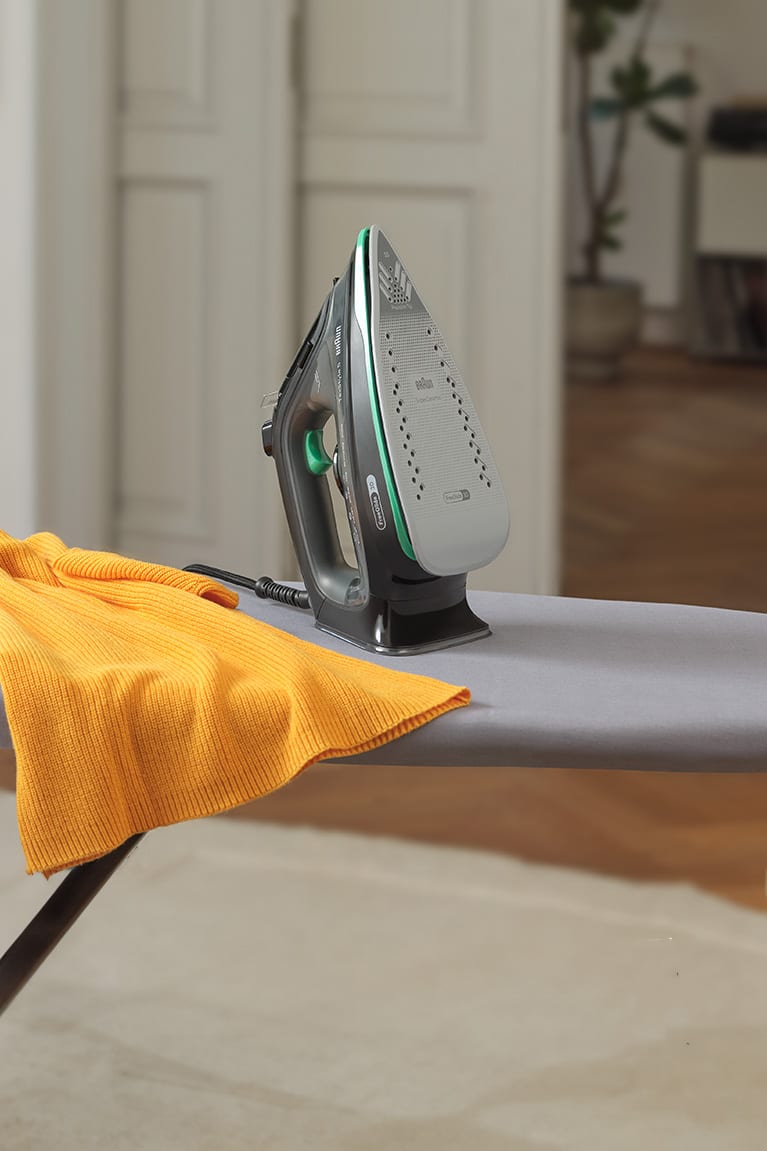 Braun TexStyle 5 Steam iron standing on an ironing board with a yellow sweater
