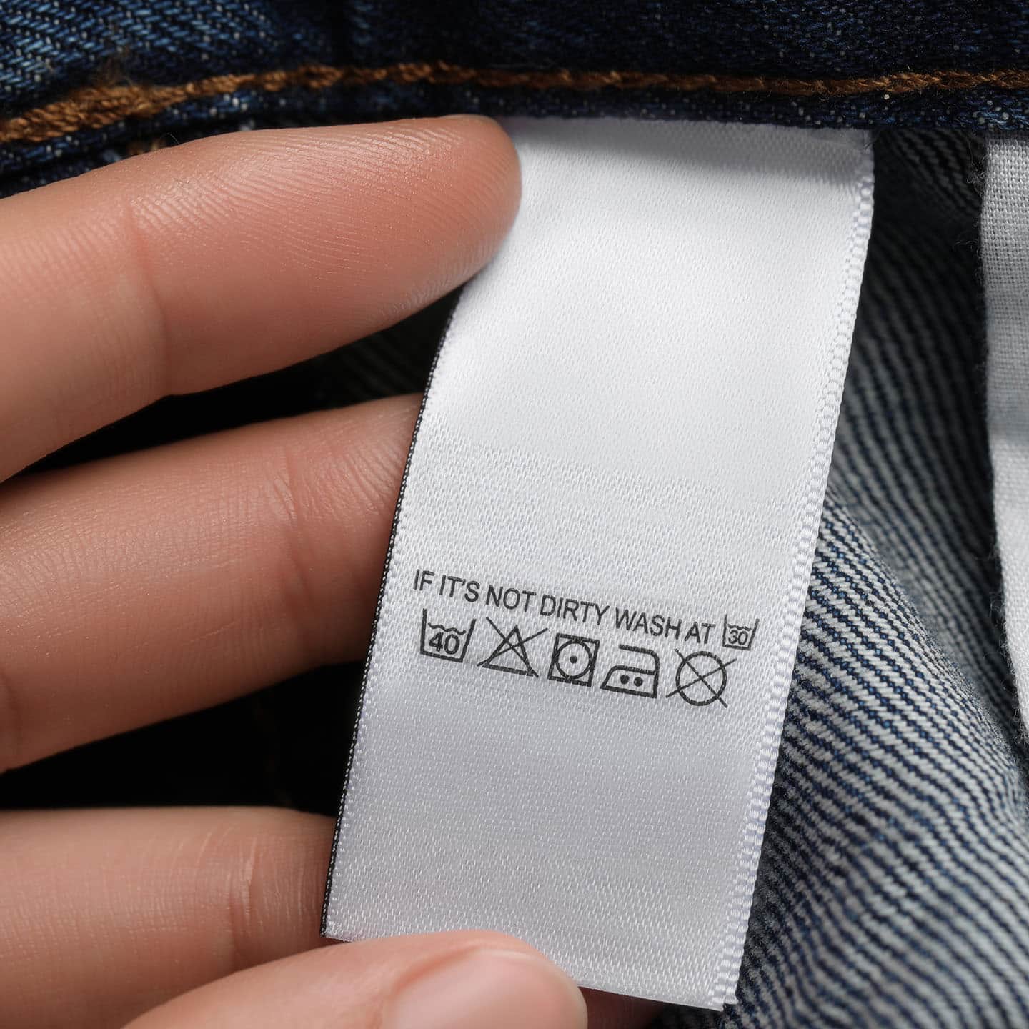 Ręka pokazująca metkę doszytą do jeansów z instrukcją prania